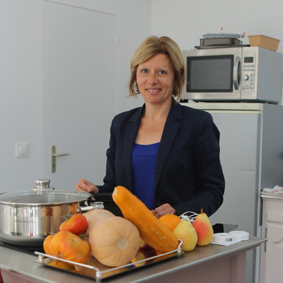 Femme dans une cuisine, avec des légumes et une casserole disposés devant elle