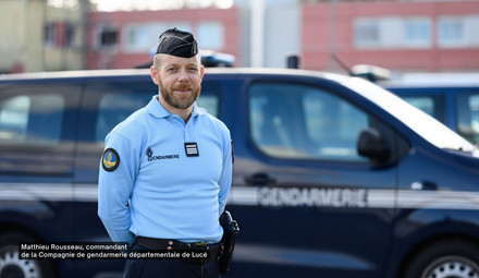 Gendarme, les mains dans le dos, devant son véhicule de fonction