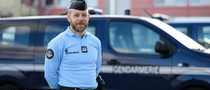Gendarme, les mains dans le dos, devant son véhicule de fonction