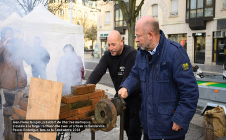 Jean-Pierre Gorges, président de Chartres métropole, s’essaie à la forge traditionnelle avec un artisan de Sandarville, Pascal Roderigue, lors de la Saint-André 2023
