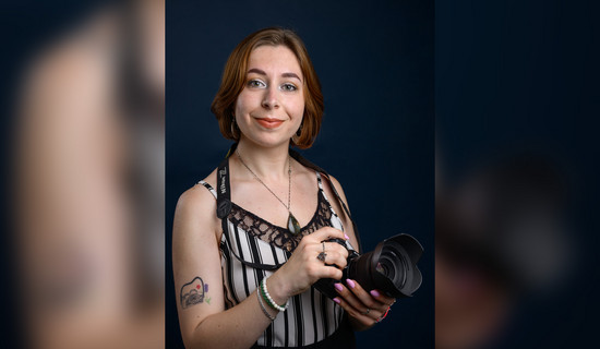 Portrait de Lucie Salmon tenant un appareil photo et montrant son tatouage au bras représentant un appareil photo